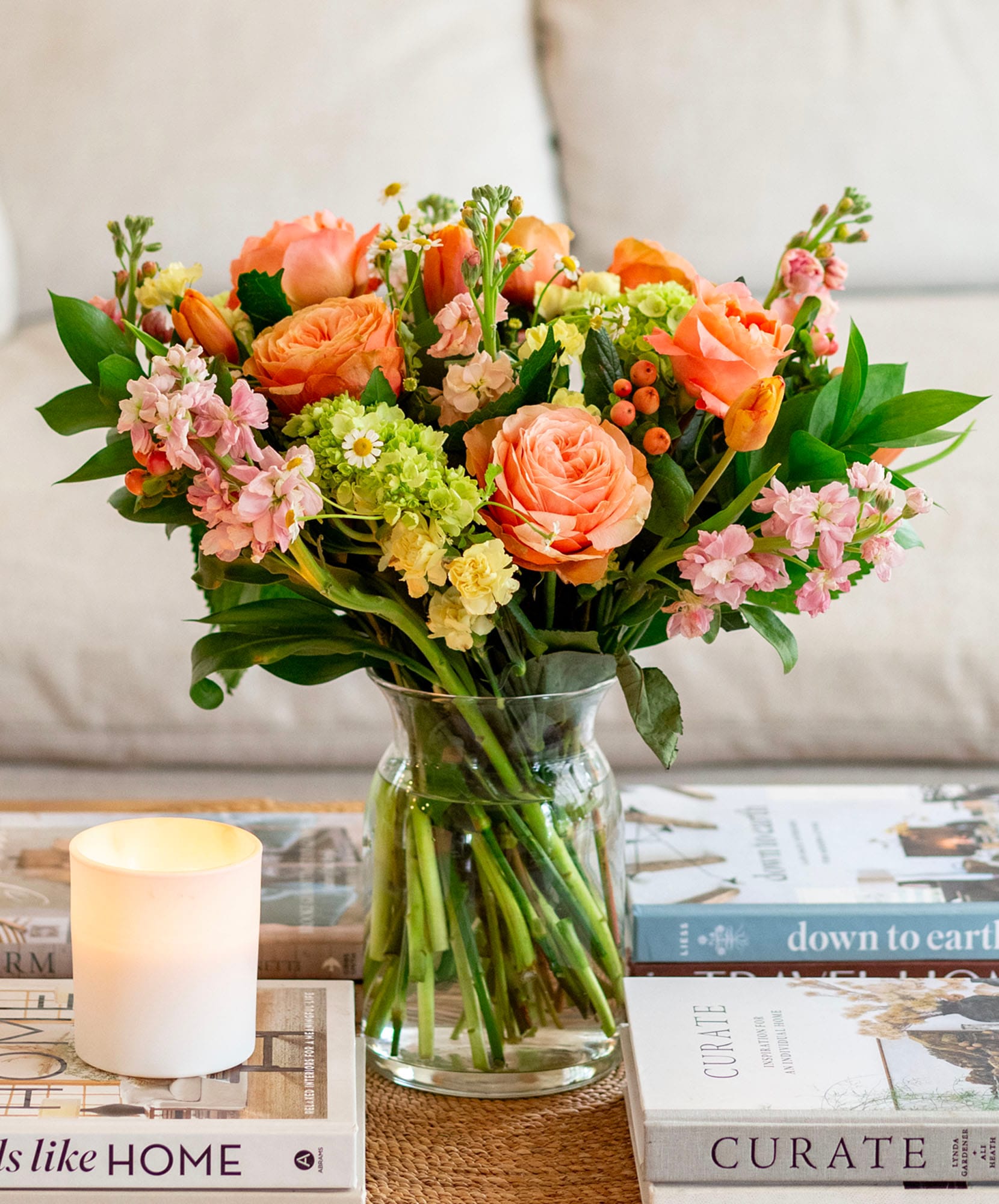 Charming flower arrangement with peach roses and bright greenery in a glass vase.